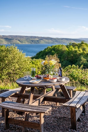 A wooden picnic table with a view of a lake and hills.
