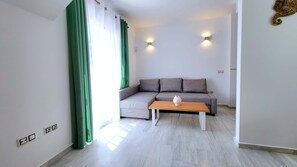Ein modernes Wohnzimmer mit einem grauen Ecksofa, einem Holztisch und einem grünen Vorhang.