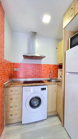 Une cuisine compacte équipée d’un lave-linge intégré, d’une hotte en acier inoxydable et d’un réfrigérateur.