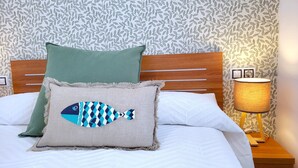 A bed with a wooden headboard, two pillows, a wall with a leafy pattern, and a bedside lamp. - Sol Suites Penthouse Plus Apartment (Fuengirola)
