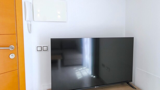 A room with a flat-screen TV on a wooden stand, a white wall, and a wooden door. - Sol Suites Penthouse Plus Apartment (Fuengirola)