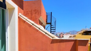 A small outdoor patio with a round table and two chairs, a green bowl on the table, and a view of a mountain in the background. - Sol Suites Penthouse Plus Apartment (Fuengirola)