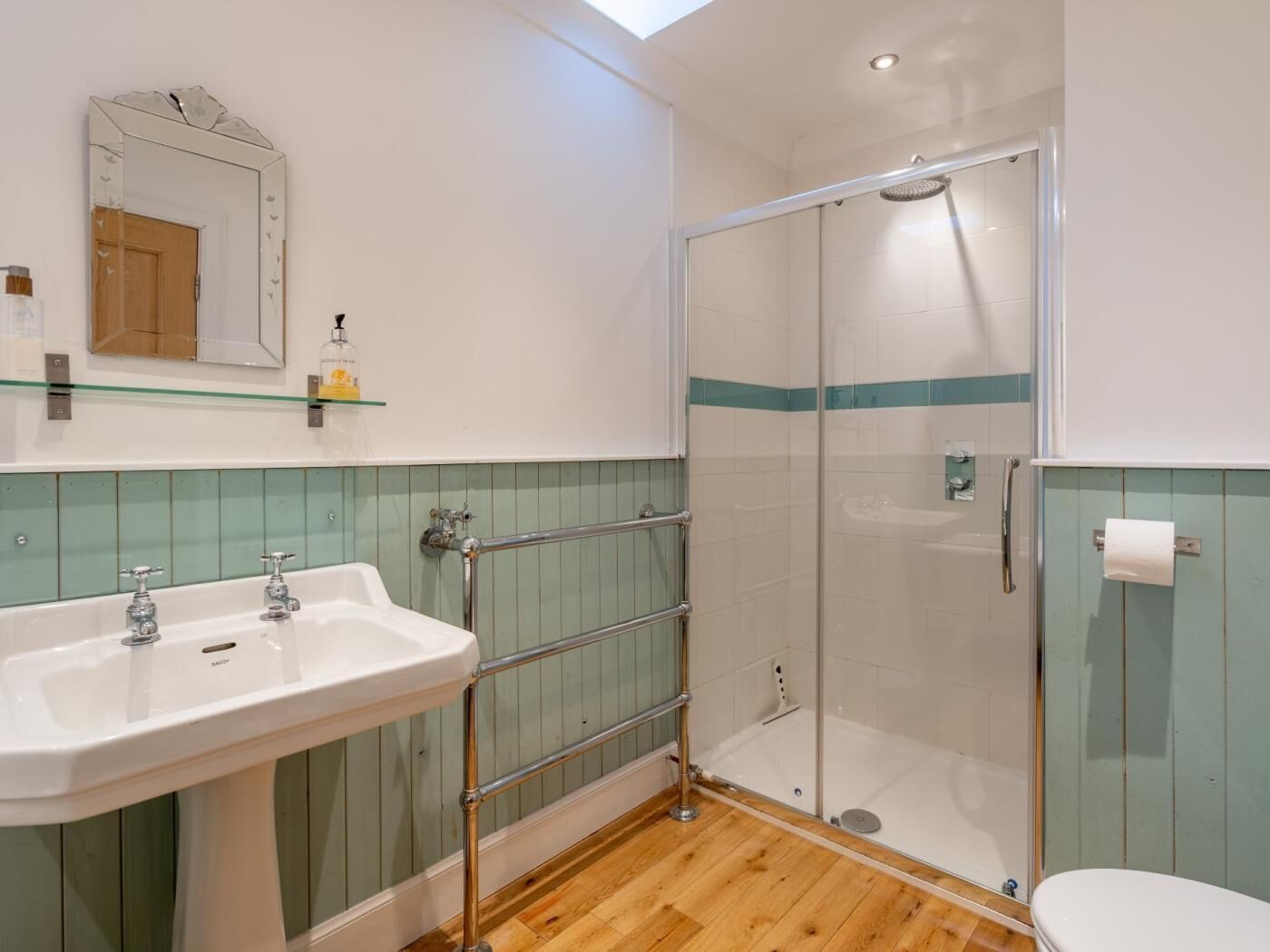A bathroom with a glass-enclosed shower, a sink with two faucets, a toilet, and a mirror with a decorative frame.
