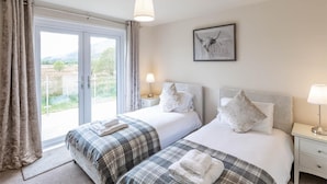 A bedroom with two beds, a large window with curtains, a framed artwork, and a bedside table with a lamp. - 2 Bed in Dalmally (oc-ca379) (Dalmally)