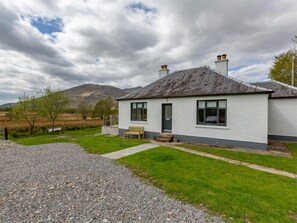 A single-story house with a gravel driveway, a wooden bench, and a view of a mountain. - 2 Bed in Dalmally (oc-ca379) (Dalmally)