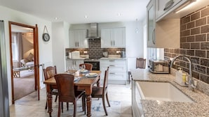 A modern kitchen with white cabinets, a brick backsplash, granite countertops, and a dining area with a wooden table and chairs. - 2 Bed in Dalmally (oc-ca379) (Dalmally)