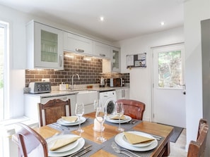 A modern kitchen with white cabinets, a brick backsplash, and a dining area with a table set for four. - 2 Bed in Dalmally (oc-ca379) (Dalmally)