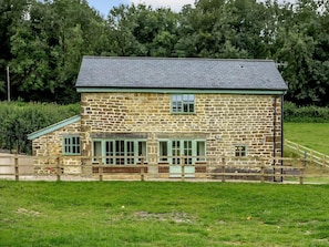 A stone building with a sloped roof, a small porch, and a fenced area. - 3 Bed in Bridport (oc-76820) (West Milton)