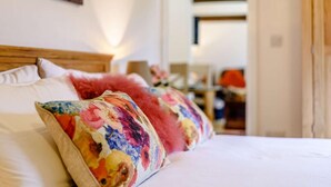 Uma cama com almofadas florais coloridas, cabeceira de madeira e um quadro na parede.