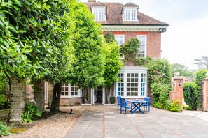 A brick house with a covered patio, a table with chairs, and a large tree in the foreground. - The Manor, Deal, Kent (Deal)