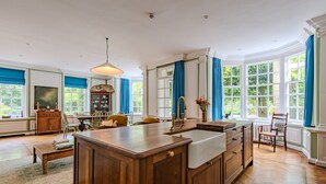 A spacious kitchen with a central island, wooden cabinetry, and large windows with blue curtains. - The Manor, Deal, Kent (Deal)