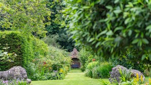 A garden pathway leading to a brick archway, surrounded by lush greenery and stone statues. - The Manor, Deal, Kent (Deal)