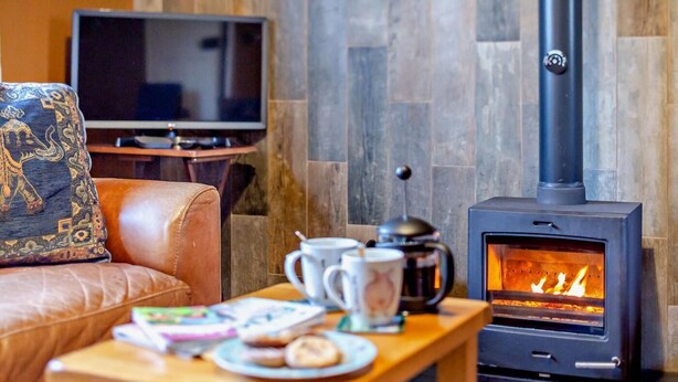 Una sala de estar acogedora con un sofá de cuero, una mesa de centro con un libro y una taza, un televisor y una chimenea de leña.