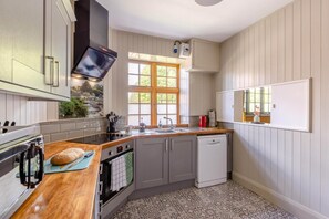 A kitchen with a wooden countertop, a built-in oven, a dishwasher, and a window with a view of greenery.