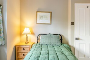 A bedroom with a bed, a nightstand with a lamp, a dresser, and a door.