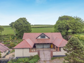 A house with a red-tiled roof, a garage, and a garden with trees and grass.