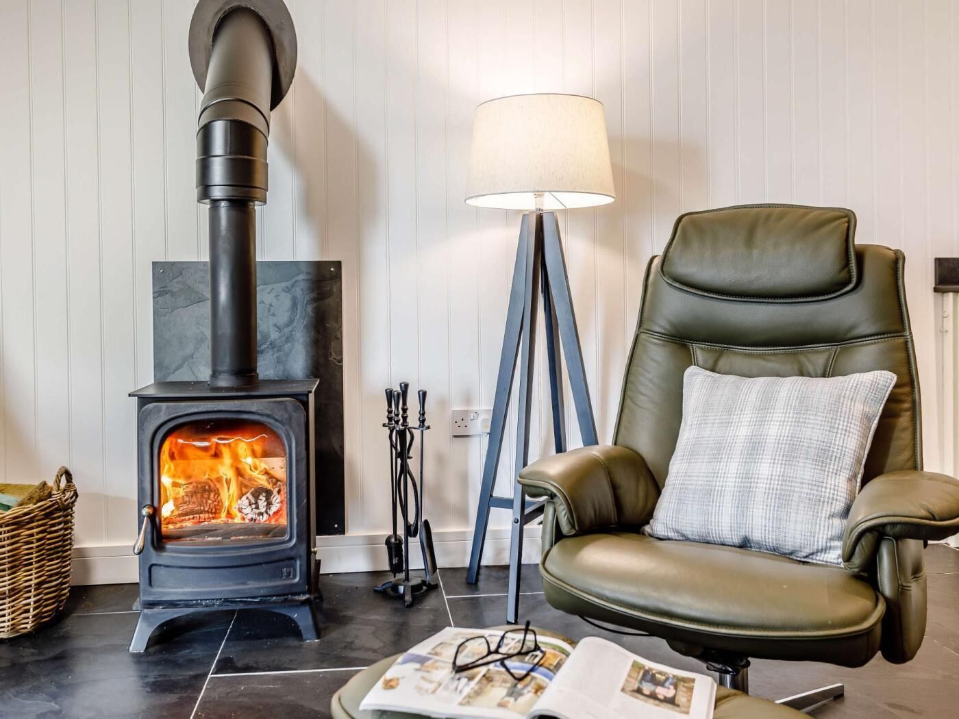Ein Zimmer mit Kaminofen, Ledersessel, Stehlampe und Korbwannen.