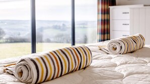 Ein Schlafzimmer mit großem Fenster, einem Bett mit gestreifter Decke und einer weißen Kommode.