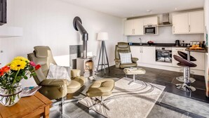 Ein modernes Wohnzimmer mit Kamin, Essbereich und Küche mit weißen Schränken und einer schwarzen Arbeitsplatte.