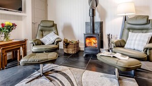 Ein gemütliches Wohnzimmer mit Kamin, Ledersesseln, einem Fernseher und einem kleinen Tisch mit Blumen.