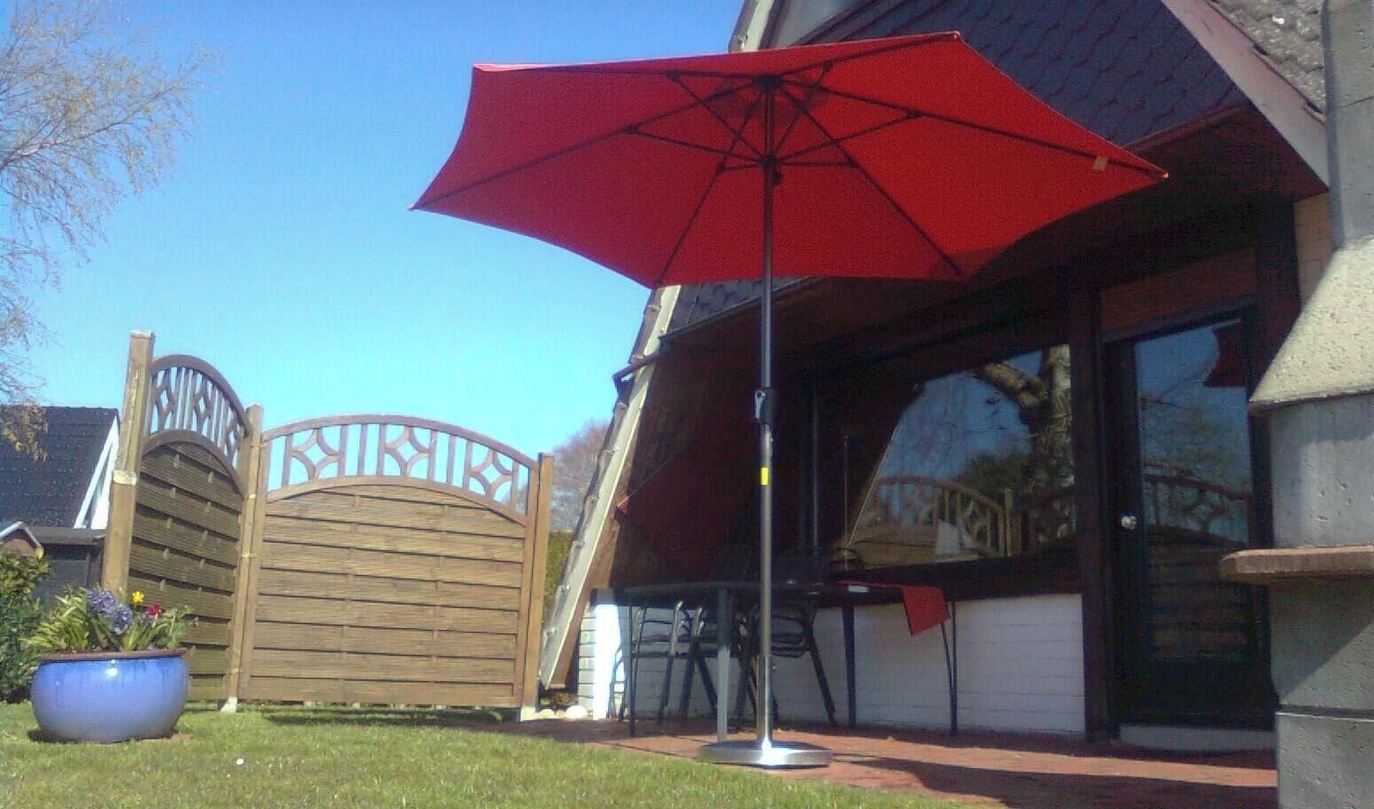 En patio med et rødt parasol, en træport og en potteplante.