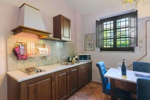 A kitchen with wooden cabinets, a stainless steel sink, a microwave, and a window with a view of greenery. - Resort Suite Giaggiolo: One-Bedroom Apartment with Garden and Pool (Bagno a Ripoli)