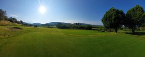 Un campo da golf con cielo sereno, montagne in lontananza e alcuni alberi.