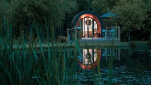 A circular building with a glass door, surrounded by trees, and reflecting in the water.