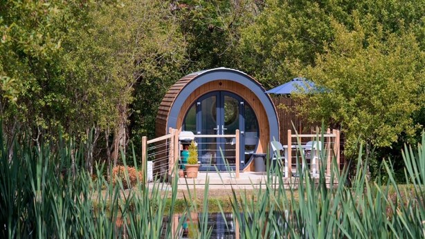 A circular building with a wooden exterior, large glass windows, and a small outdoor seating area.