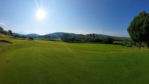 Un campo de golf con cielo despejado, montañas a lo lejos y algunos árboles.