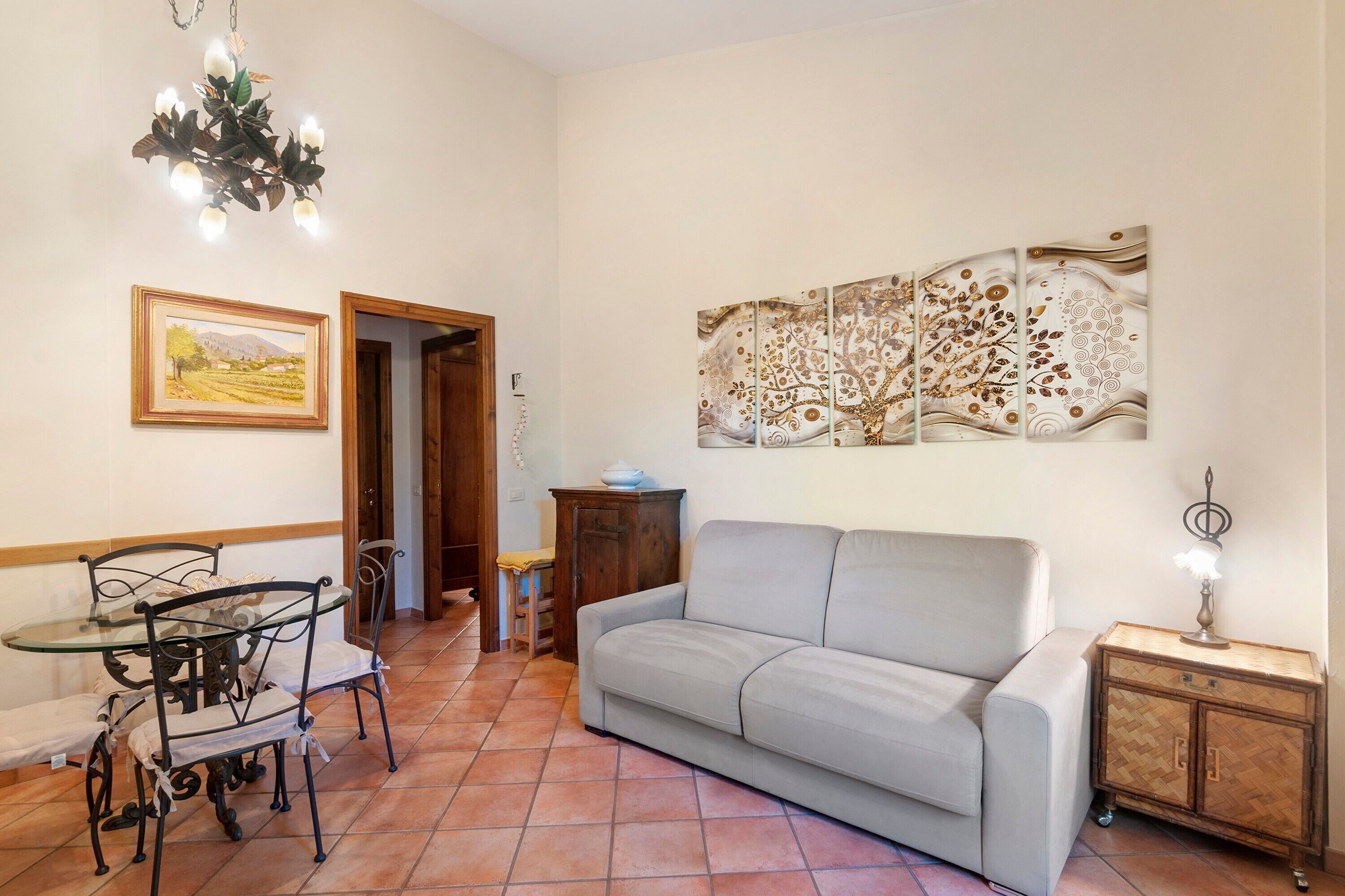 Una sala de estar con un sofá, una mesa de comedor con sillas, una araña y una pared con un cuadro abstracto de gran tamaño.