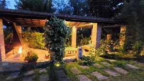 Un espacio al aire libre techado con una chimenea, sendero de piedra y follaje.