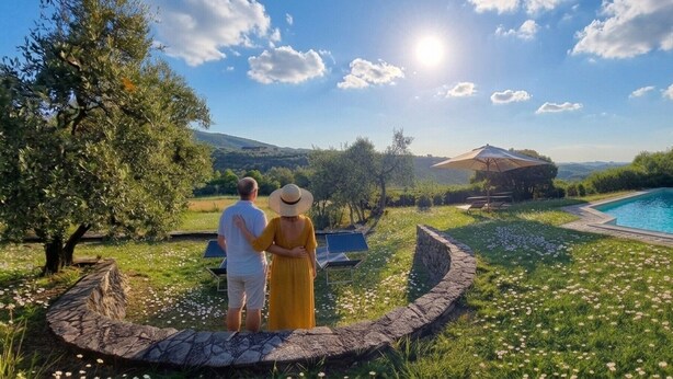 Una pareja de pie junto a una piscina con un muro de piedra y vistas al campo.