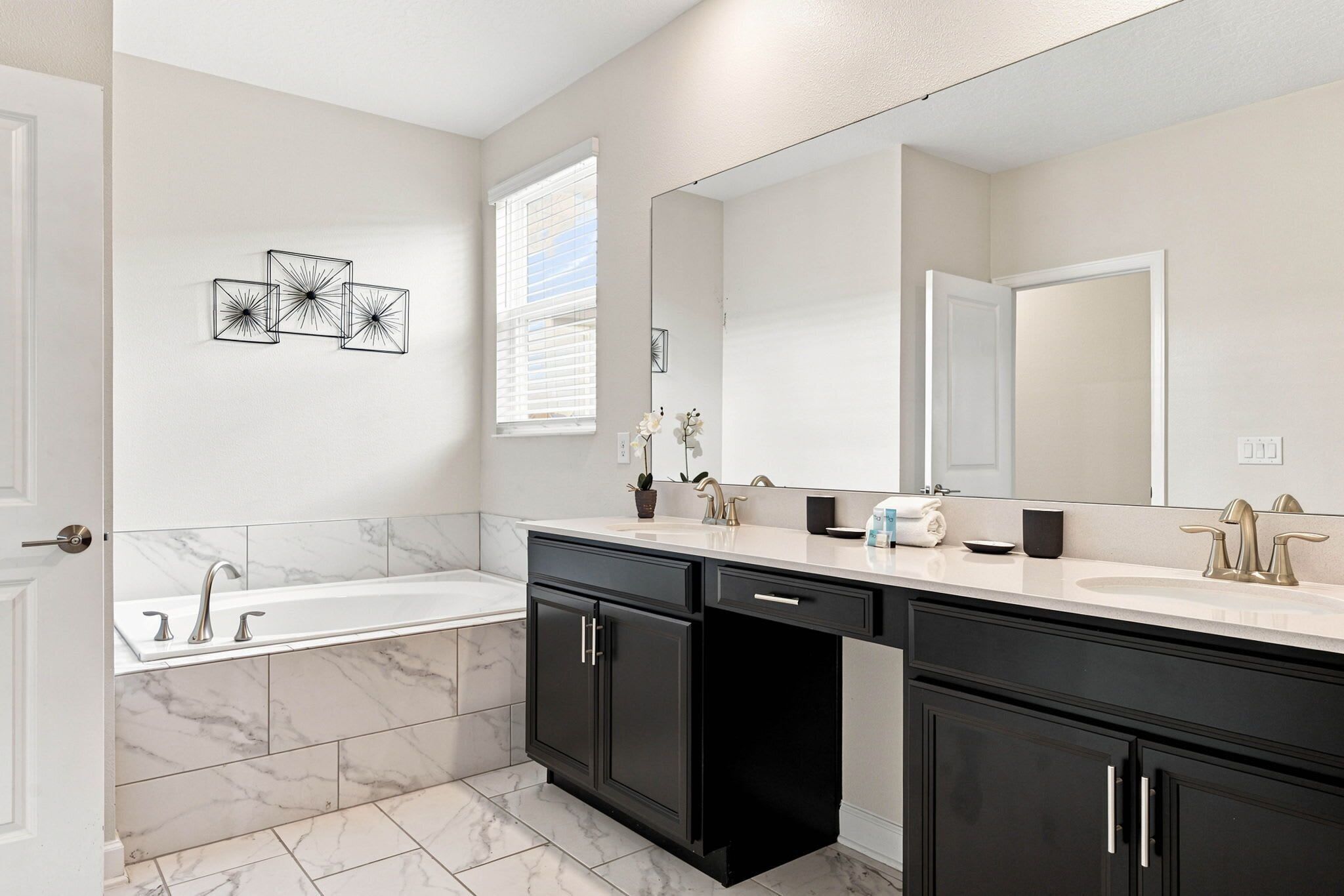 A modern bathroom with a bathtub, double sink, and large mirror.