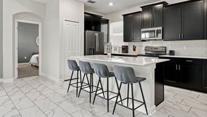 A modern kitchen with dark cabinets, a white island, and bar stools. - 5BR ChampionsGate Home w/ Pool & Theme Rooms (Kissimmee)