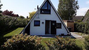 Een wit, driehoekig huis met een zwarte deur, een klein raam en een schotelantenne.