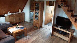 Een gezellige woonkamer met een houten bank, een salontafel, een tv-meubel en een trap naar een slaapkamer op de entresol.