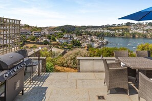An outdoor patio with a grill, wicker furniture, and a view of a town and water body. - 5 Bed in Fowey (oc-77657) (Polruan)