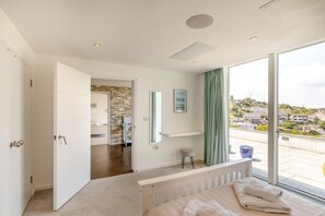 A bedroom with a large window, a bed, a bathroom with a stone wall, and a view of the city. - 5 Bed in Fowey (oc-77657) (Polruan)