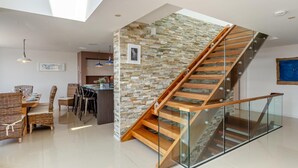 Ein modernes Interieur mit einer Glasstufenwendeltreppe, einem Essbereich mit Korbmöbeln und einer Küche im Hintergrund.