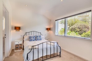 A bedroom with a bed, two bedside tables, a window with blinds, and a wall-mounted light fixture. - 5 Bed in Fowey (oc-77657) (Polruan)