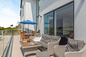 An outdoor seating area with a sofa, chairs, and a table, featuring a large window and a blue umbrella. - 5 Bed in Fowey (oc-77657) (Polruan)