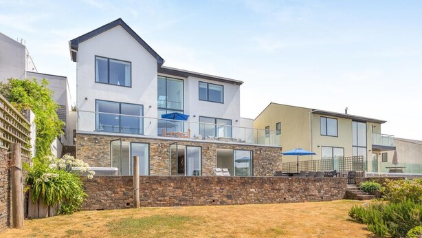 Ein modernes, zweistöckiges Haus mit Steinverkleidung, großen Fenstern und einem Balkon mit Gartenmöbeln.