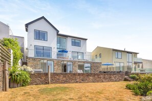 A modern two-story house with a stone facade, large windows, and a balcony with outdoor furniture. - 5 Bed in Fowey (oc-77657) (Polruan)