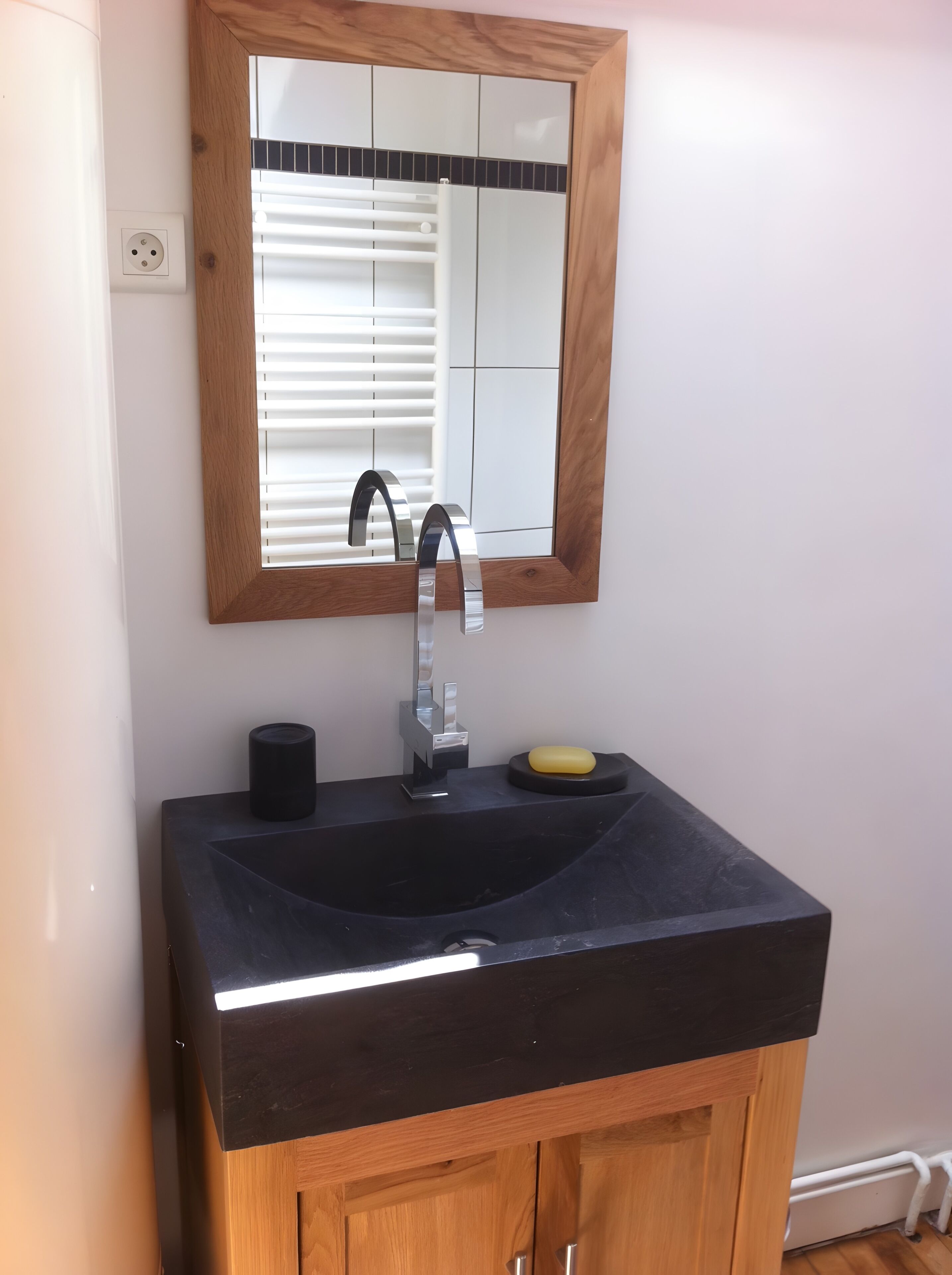 A bathroom with a black sink, a wooden cabinet below, a mirror with a wooden frame, and a window with blinds.