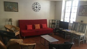 Ein Wohnzimmer mit einem roten Sofa, Korbsesseln, einem Fernseher und einer Wanduhr.