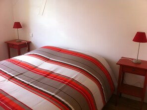 Un lit recouvert d’une couverture à rayures, deux tables de chevet avec des lampes et un mur blanc.