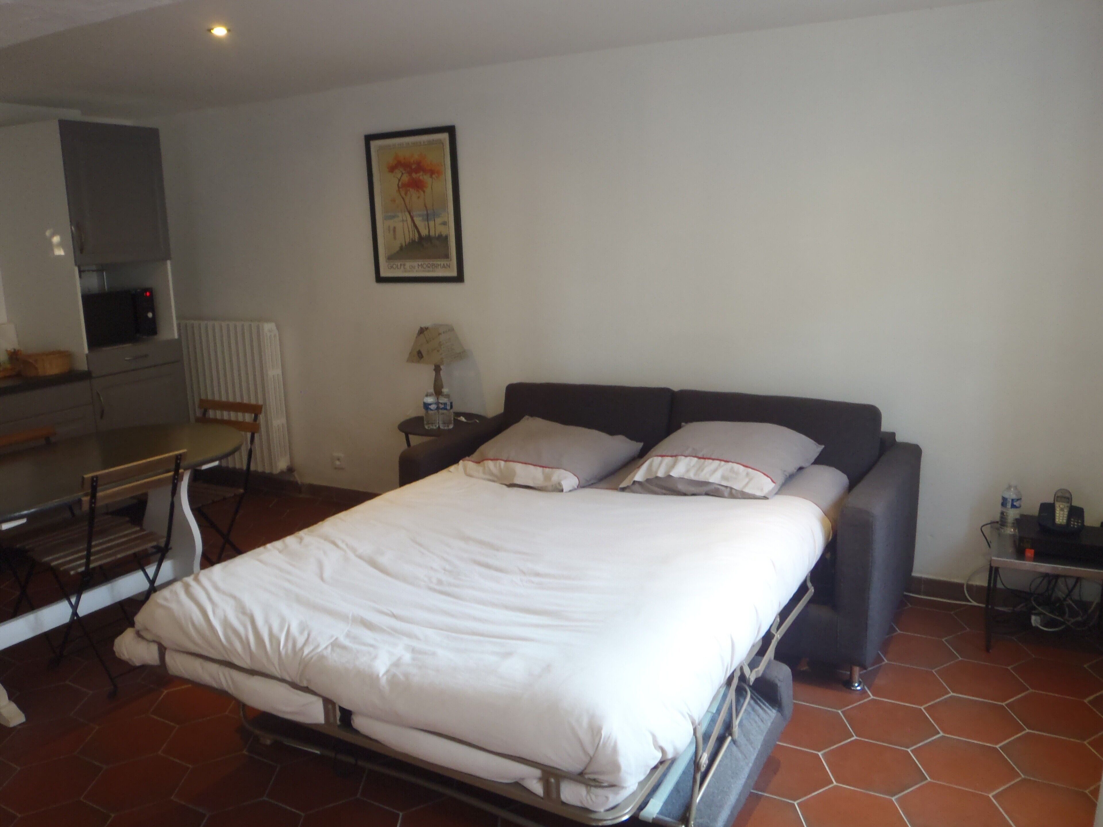 A bedroom with a bed, a desk, a chair, a lamp, and a picture on the wall.