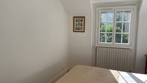 Ein Zimmer mit einem Bett, einem Fenster mit Blick auf Grünflächen, einem Heizkörper und einem gerahmten Bild an der Wand.