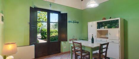 A dining area with a table and chairs, a white cabinet with glassware, and a door leading outside.
